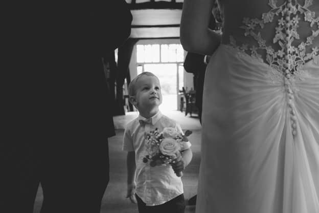 The bride's young son looking up at his mum in her wedding dress, holding a small bouquet. Captured in a black-and-white photograph by Chris Stephenson Photography, highlighting a tender, candid moment.