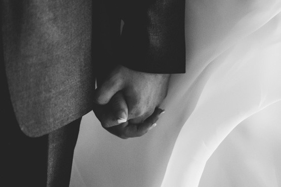 Close-up of a bride and groom holding hands, showcasing their wedding rings. Captured in a black-and-white photograph by Chris Stephenson Photography, highlighting the intimate, tender moment.