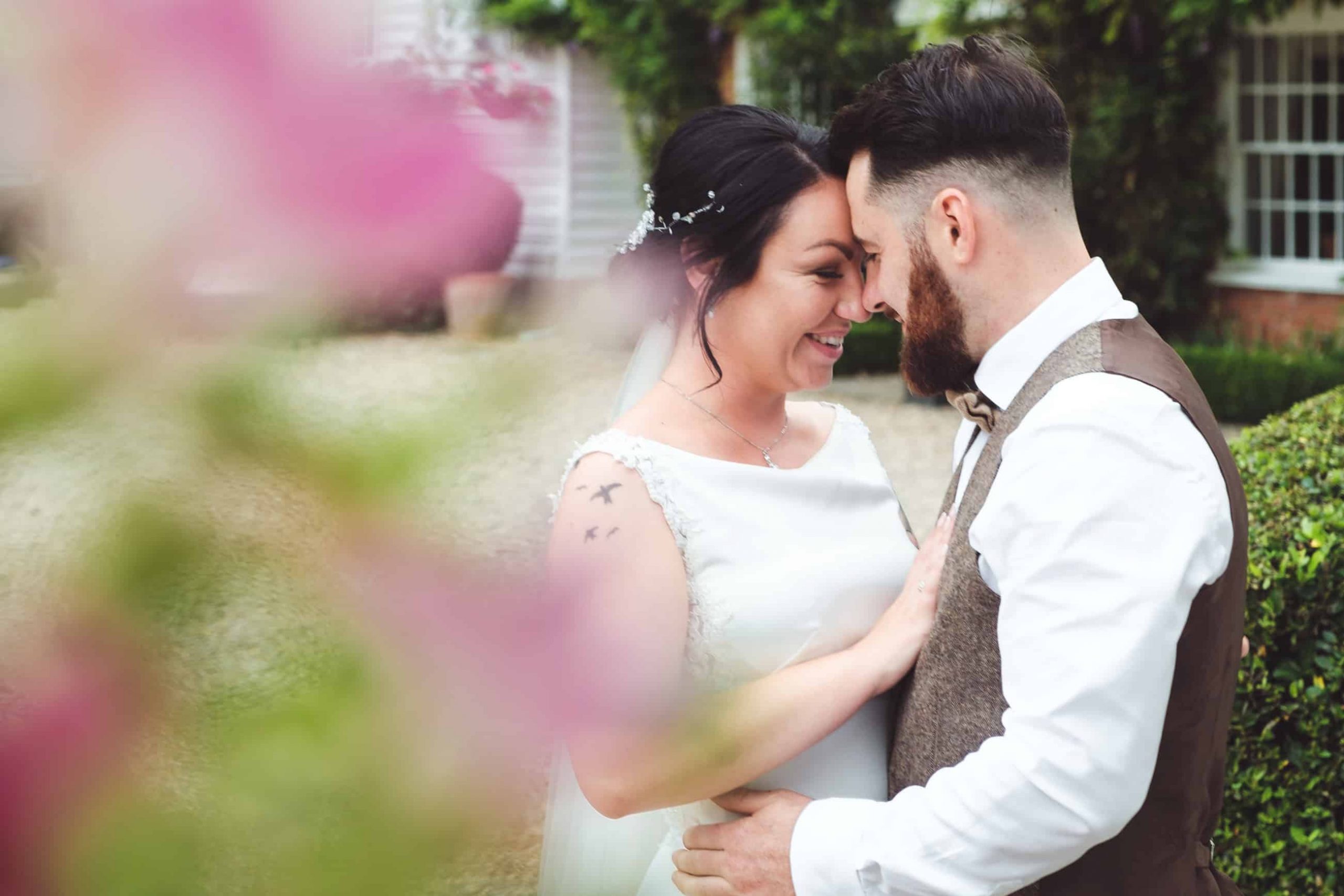 Bride and groom sharing an intimate moment outdoors, with the bride gently placing her hand on the groom's chest. Captured by Chris Stephenson Photography in a relaxed, candid style with soft focus on the surrounding garden.