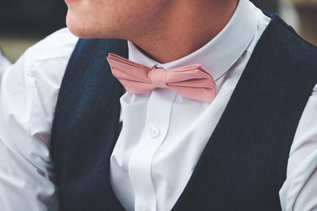 Close-up of a groom wearing a white shirt, navy vest, and a pink bow tie. Captured by Chris Stephenson Photography, highlighting the elegant wedding attire.