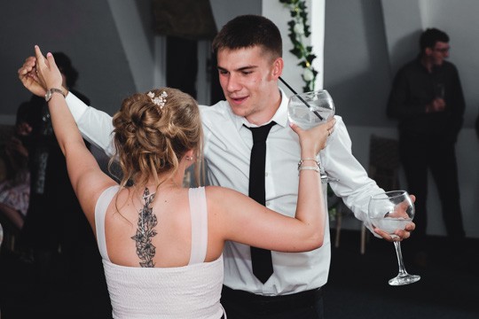 Wedding guests dancing and enjoying the celebration. A woman with a back tattoo and an elegant updo is dancing with a man in a white shirt and black tie. Captured by Chris Stephenson Photography in a lively, candid style.